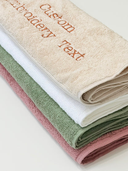 Personalized cotton bath towel embroidered with custom name in beige, white, green and dark pink colors.